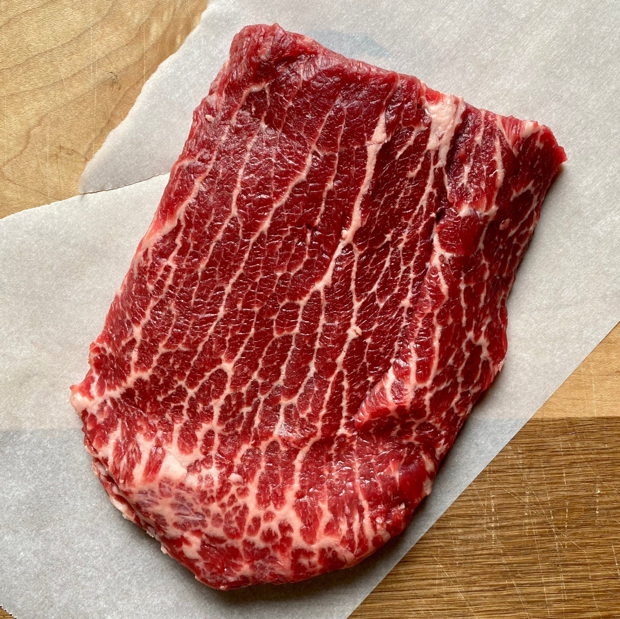 A flat iron steak with a bold, marbled texture, resting on a piece of parchment paper.
